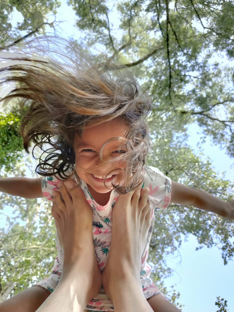 Léonie, portée en l'air par son papa, éclatante de rire, les cheveux au vent